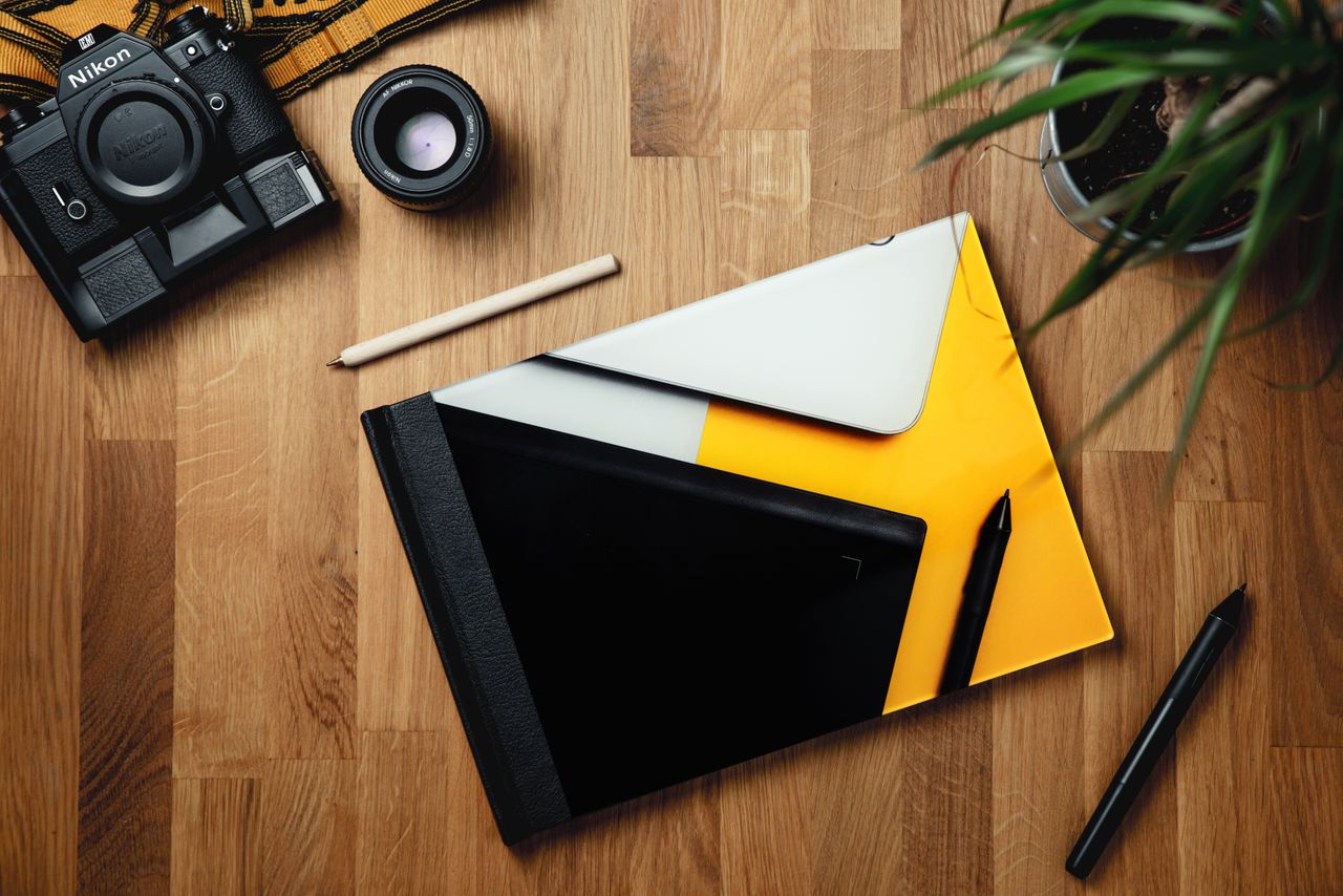 project-02-a Top view of colorful rectangular notebook surrounded by pens and pot plant composing with professional photo camera and lens on wooden table in bright room